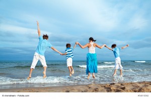 Happy Mother and three sons are jumping on beach